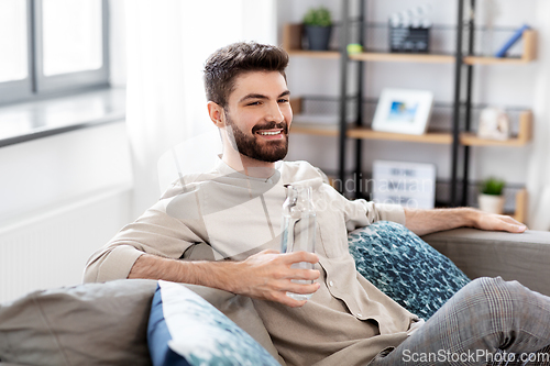 Image of happy man drinking water from glass bottle at home