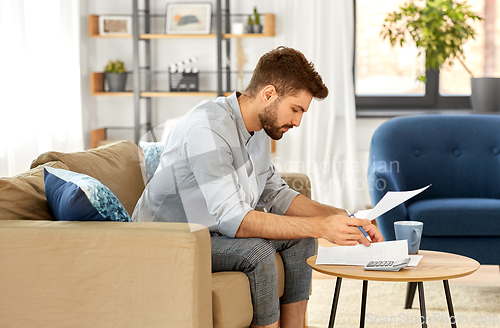 Image of man with bills counting on calculator at home