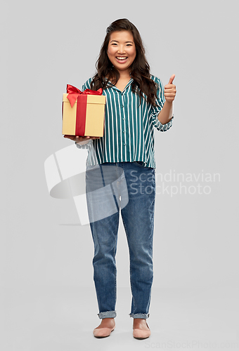 Image of happy asian woman with gift box showing thumbs up