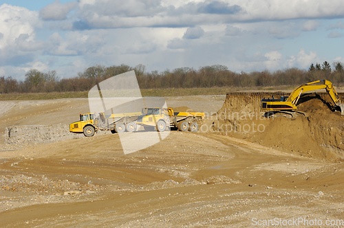 Image of Yellow dump trucks and excavator are working in gravel pit