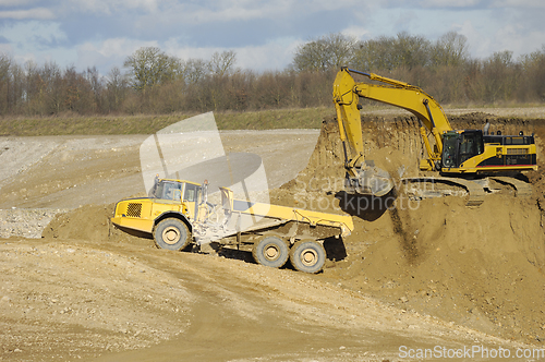 Image of Yellow dump trucks and excavator are working in gravel pit