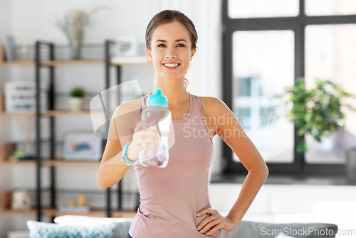 Image of smiling young woman with bottle of water at home