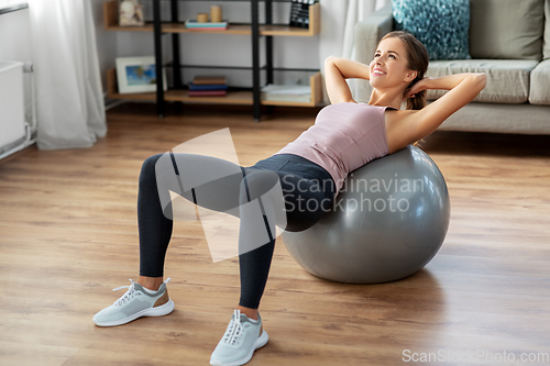 Image of happy woman exercising on fitness ball at home