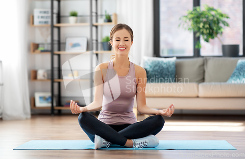 Image of woman doing yoga in lotus pose at home