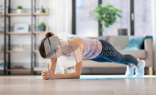 Image of young woman doing plank exercise on mat at home