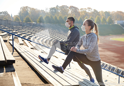 Image of couple in masks stretching leg on stadium