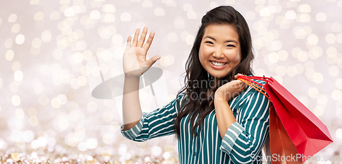 Image of happy asian woman with shopping bags waving hand