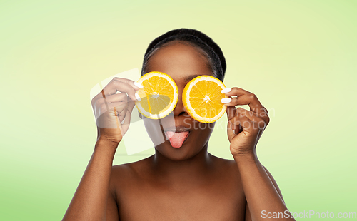 Image of african woman making eye mask of oranges