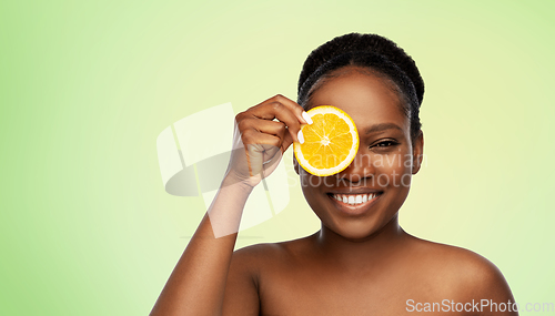 Image of smiling african woman making eye mask of oranges