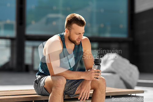 Image of tired sportsman with bottle sitting on city bench