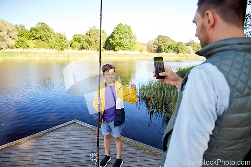 Image of father photographing son with fishing rod on river