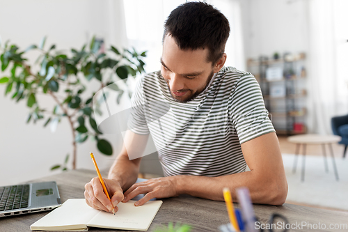 Image of man with notebook and laptop at home office