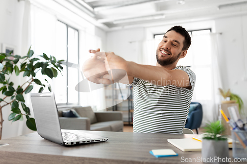 Image of happy man with laptop stretching at home office