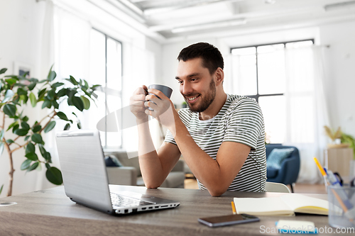 Image of man with laptop drinking coffee at home office