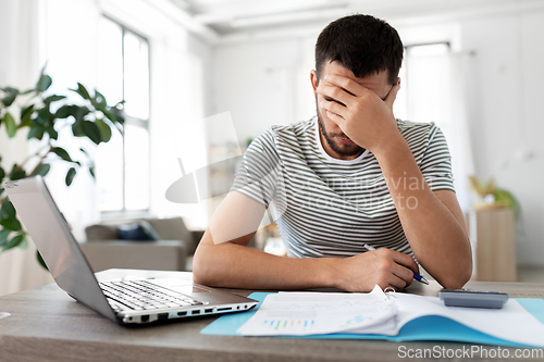 Image of man with papers and laptop working at home office