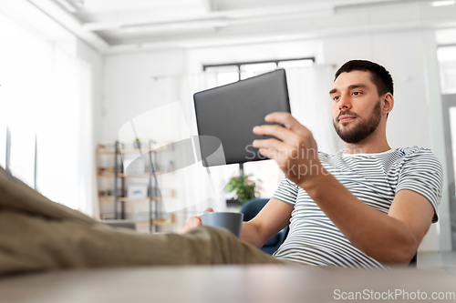 Image of man with tablet pc resting feet on table at home