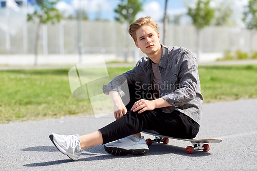 Image of teenage boy sitting on skateboard on city street