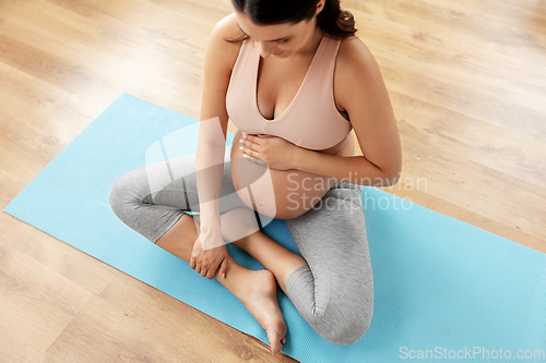 Image of happy pregnant woman sitting on yoga mat at home