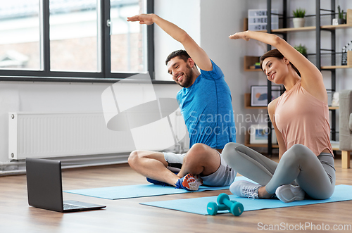 Image of happy couple with laptop exercising at home