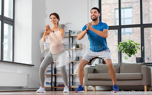 Image of happy couple exercising and doing squats at home