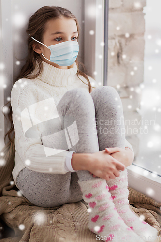 Image of sad girl in medical mask sitting on sill at home