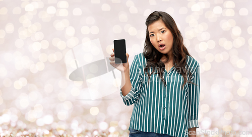 Image of shocked asian woman with smartphone over lights