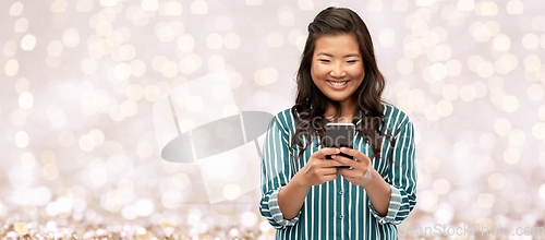 Image of happy asian woman using smartphone over lights