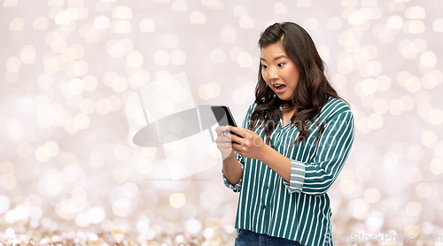 Image of surprised asian woman using smartphone over lights