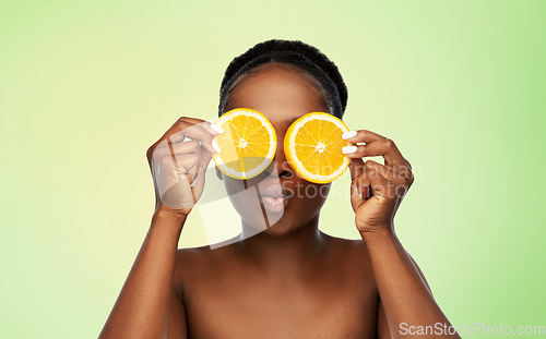 Image of african woman making eye mask of oranges