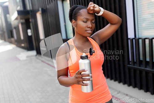 Image of tired african american woman with bottle of water