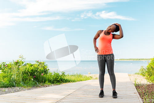 Image of young african american woman stretching on beach