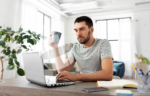 Image of man with laptop drinking coffee at home office