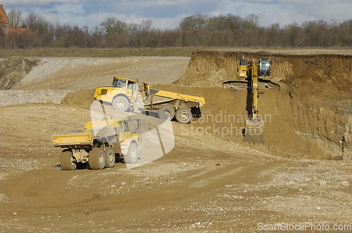 Image of Yellow dump trucks and excavator are working in gravel pit