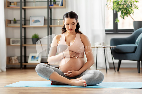 Image of happy pregnant woman sitting on yoga mat at home