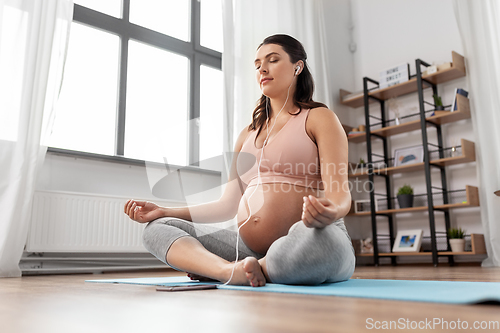 Image of pregnant woman with earphones doing yoga at home