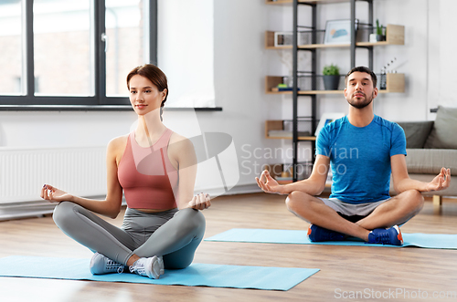 Image of couple meditating in yoga lotus pose at home