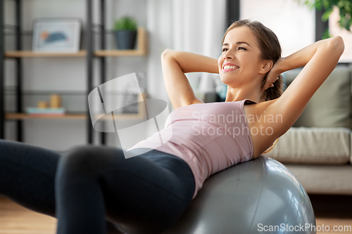 Image of happy woman exercising on fitness ball at home