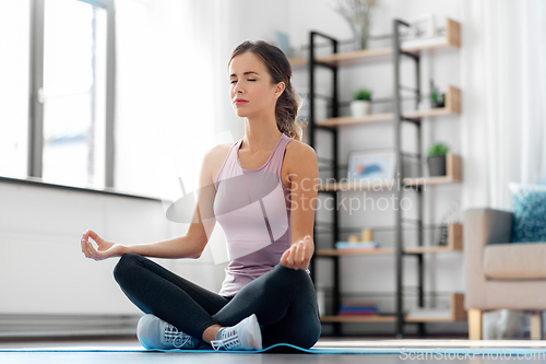 Image of woman doing yoga in lotus pose at home