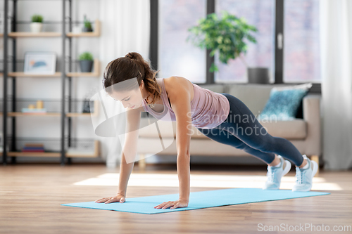 Image of young woman doing plank exercise on mat at home