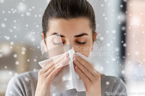 Image of sick woman blowing nose in paper tissue at home