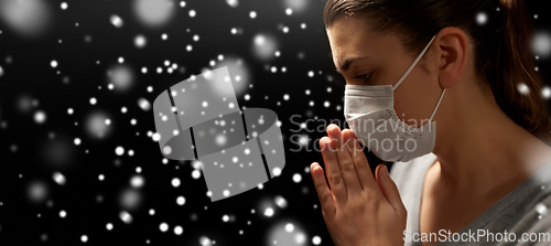 Image of sick young woman in protective face mask praying