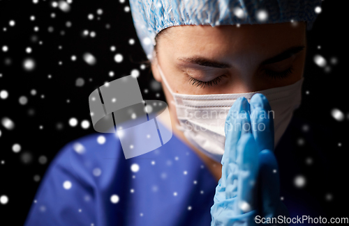 Image of female doctor or nurse in face mask praying