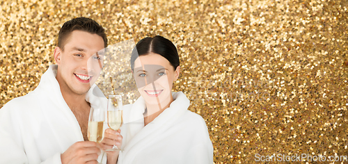 Image of happy couple in spa bath robes drinking champagne