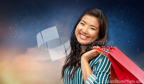 Image of happy asian woman with shopping bags on night sky