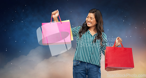 Image of happy asian woman with shopping bags on night sky