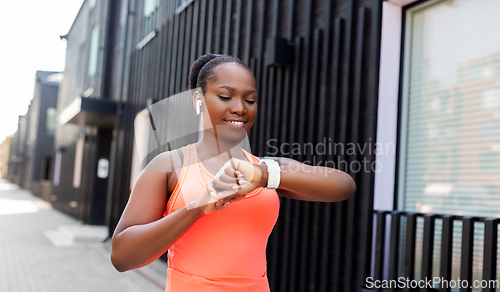 Image of happy african woman with earphones and smart watch