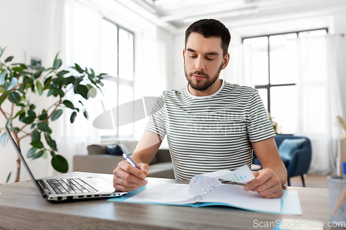 Image of man with papers and laptop working at home office