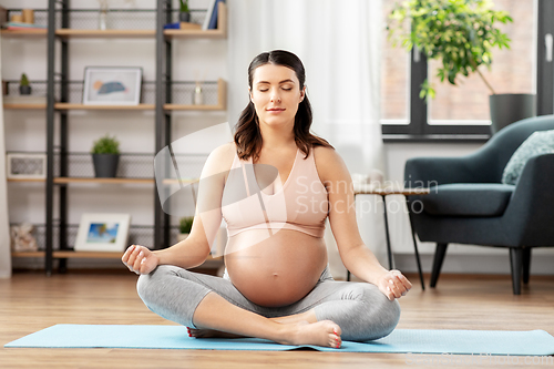 Image of pregnant woman with earphones meditating at home