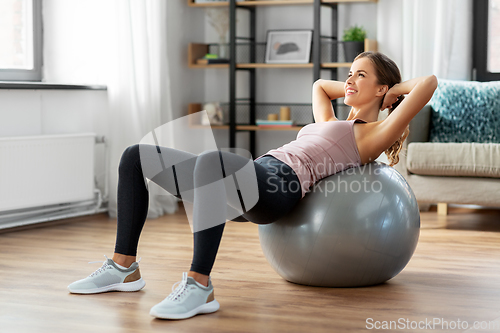 Image of happy woman exercising on fitness ball at home