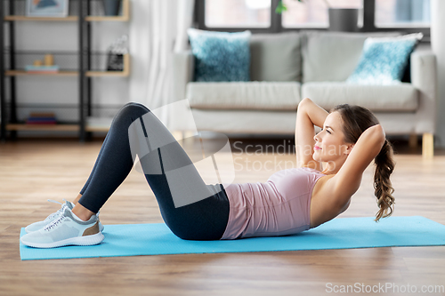 Image of young woman exercising and doing sit-ups at home